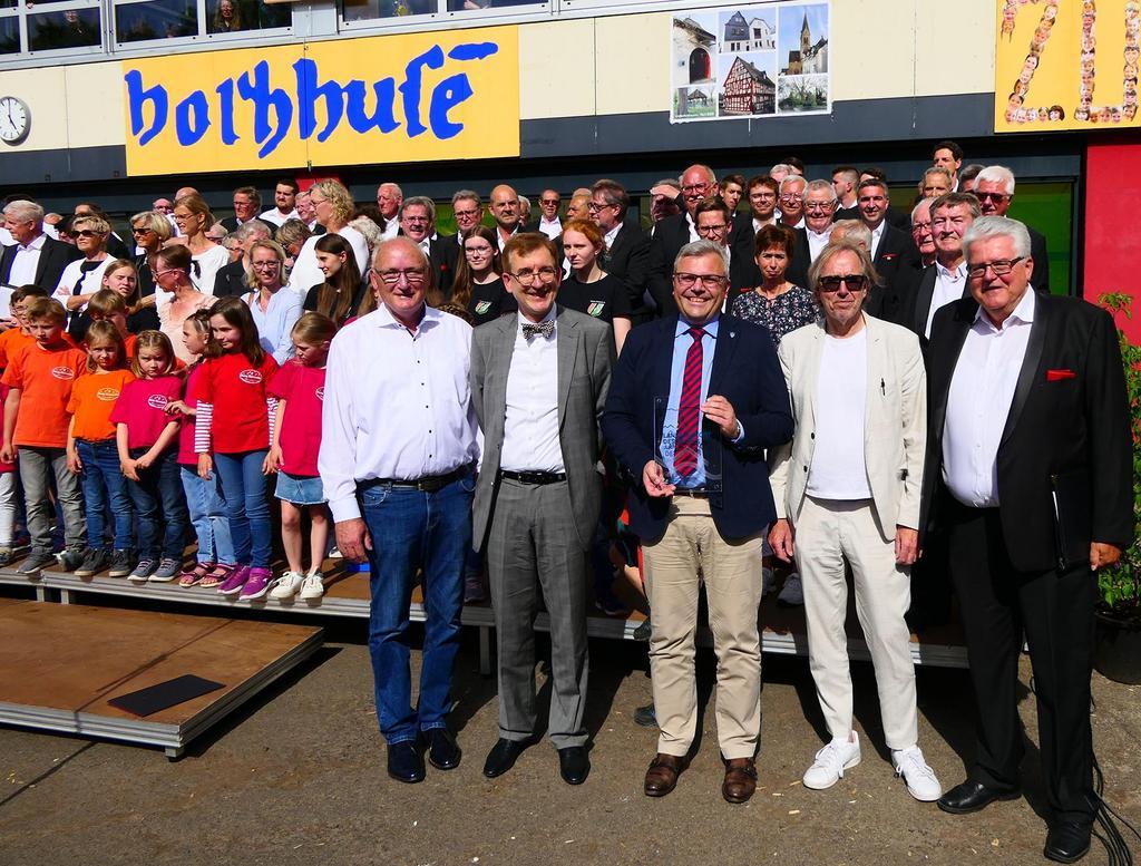  Preisverleihung zum Jubiläumsauftakt in Lindenholzhausen (vordere Reihe von rechts) Manfred Neunzerling, Prof. Udo Dahmen, Bürgermeister Dr. Marius Hahn, Dr. Tilman Schlömp und Hans-Joachim Schupp mit zahlreichen Sängerinnen und Sängern auf der Bühne. 
