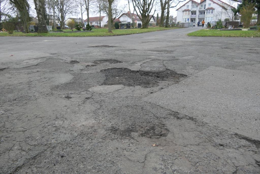Auf allen Friedhöfen, das Bild zeigt den Platz vor der Friedhofshalle in Offheim, weisen die Aspaltdecken der Wege deutliche Schäden auf. 